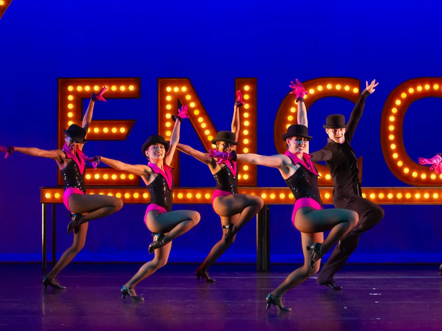 ETAP dancers in black top hats and pink costumes kicking in a line in front of the lit ENCORE marquee.