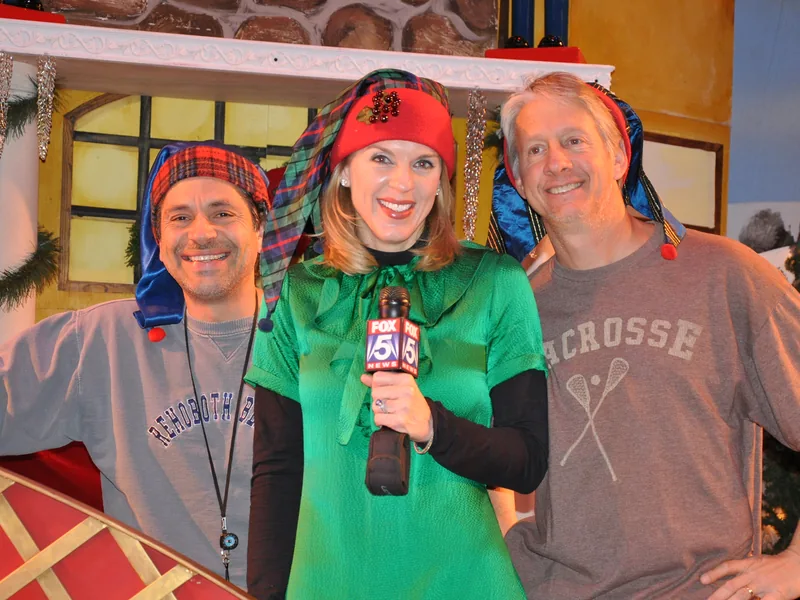 A Fox 5 News reporter in an elf hat holds a microphone on the ETAP holiday set